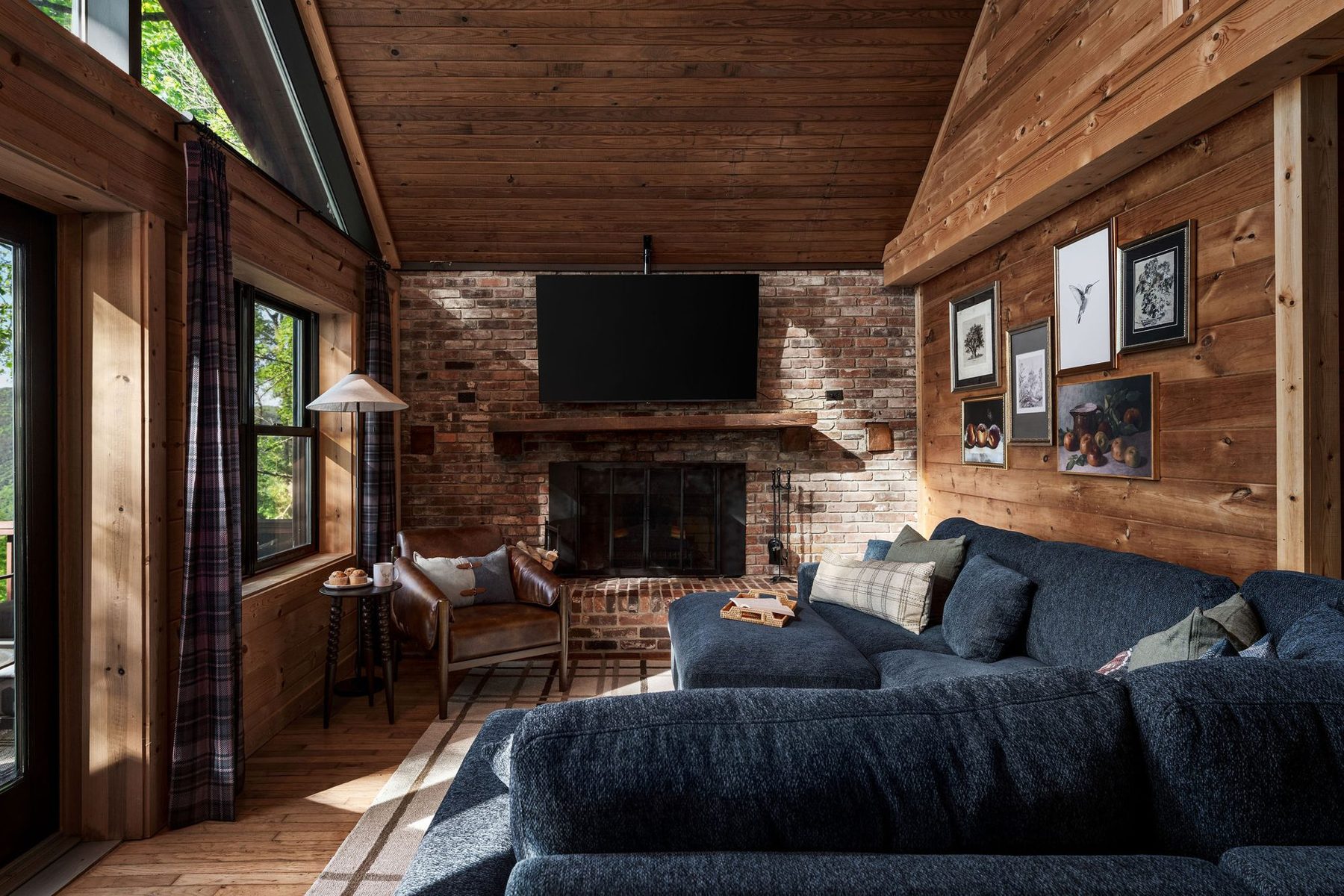 Living room: deep navy sectional facing a brick fireplace, with plaid accents and warm pine walls