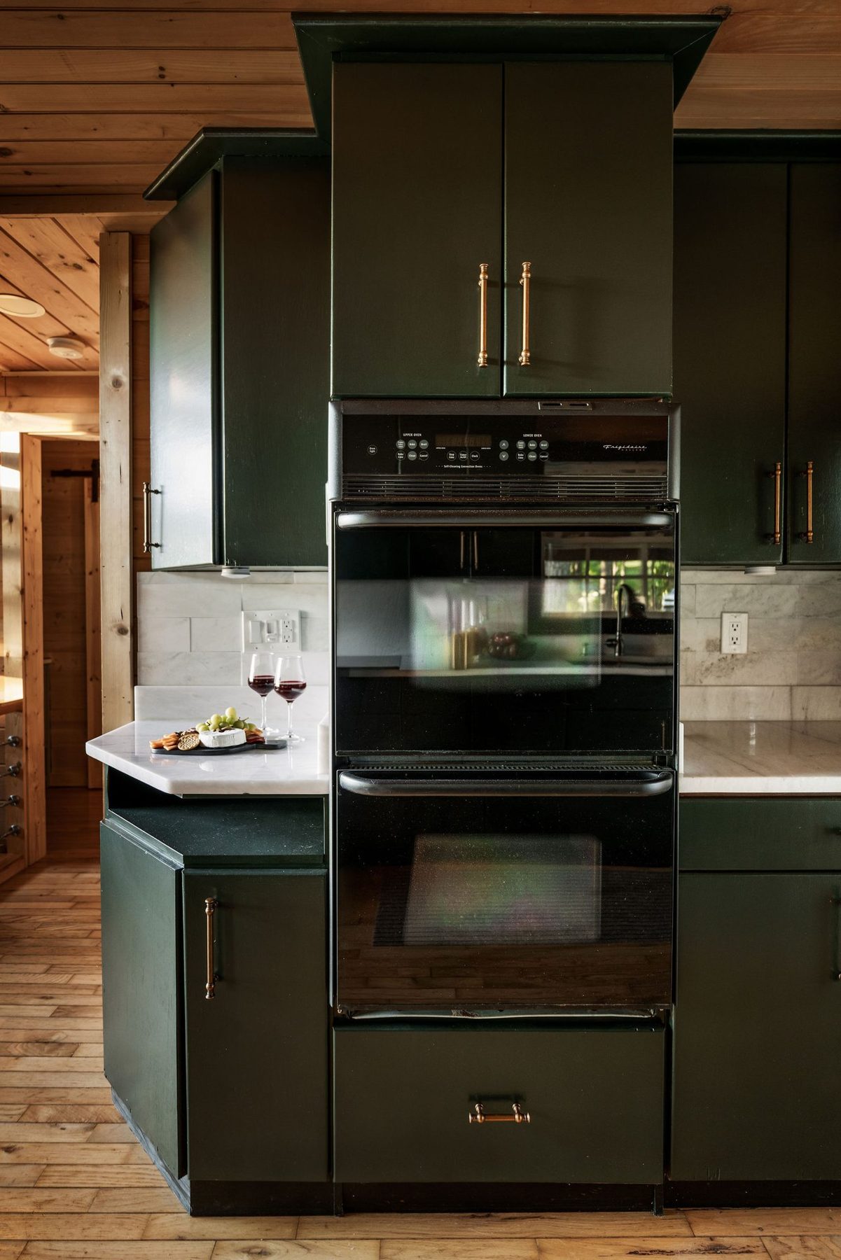 Green kitchen cabinetry with built-in double ovens and brass hardware