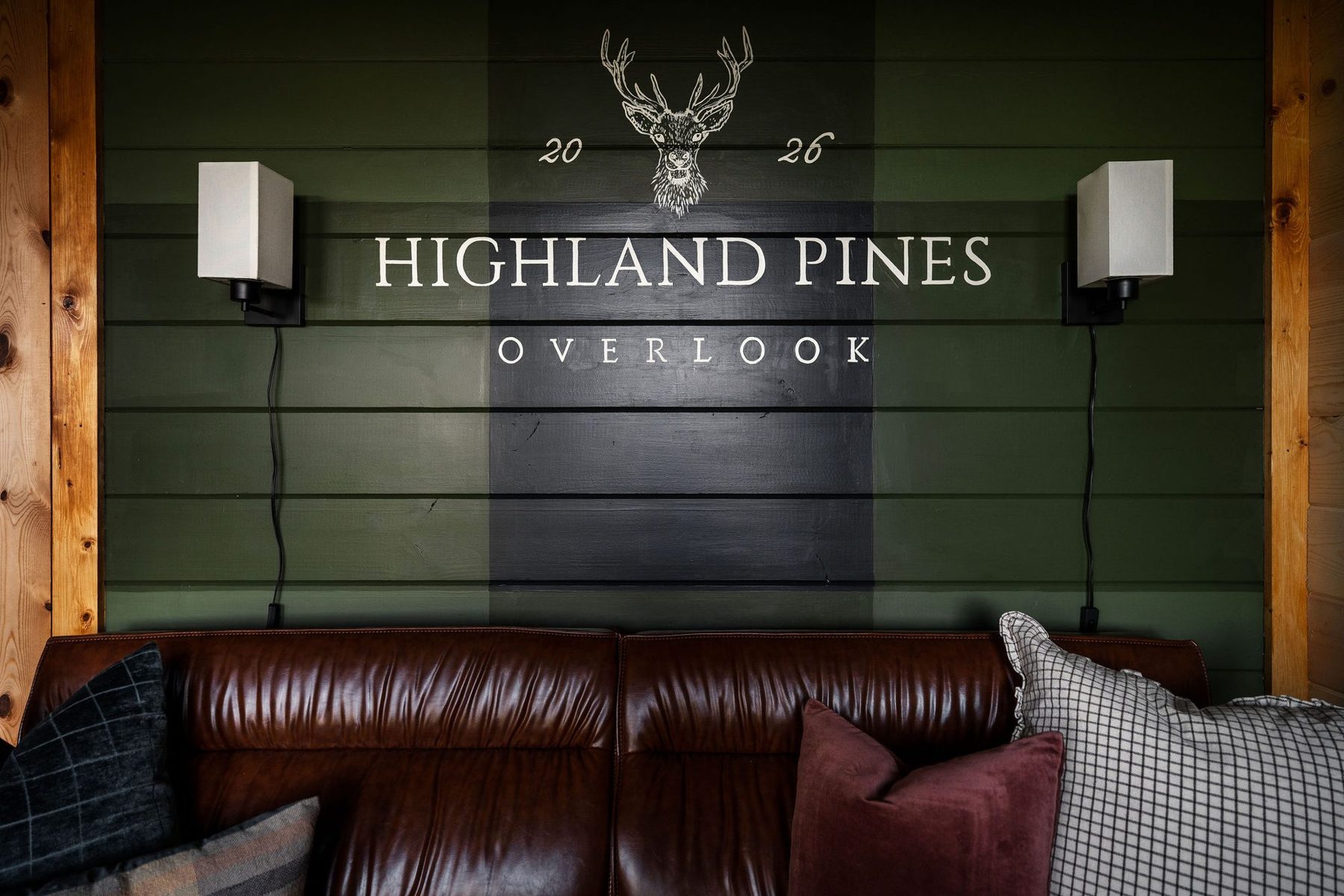 Feature wall in forest green with the Highland Pines Overlook logo above a cognac leather sofa