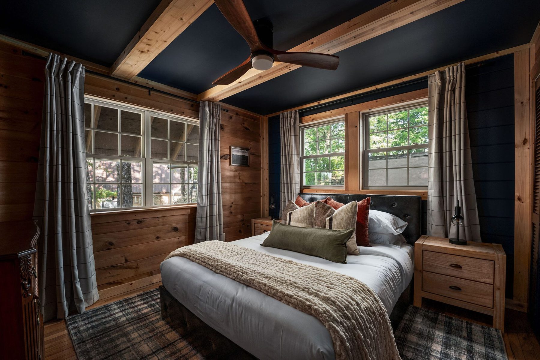 Primary bedroom under a navy coffered ceiling, layered neutral bedding and plaid rug