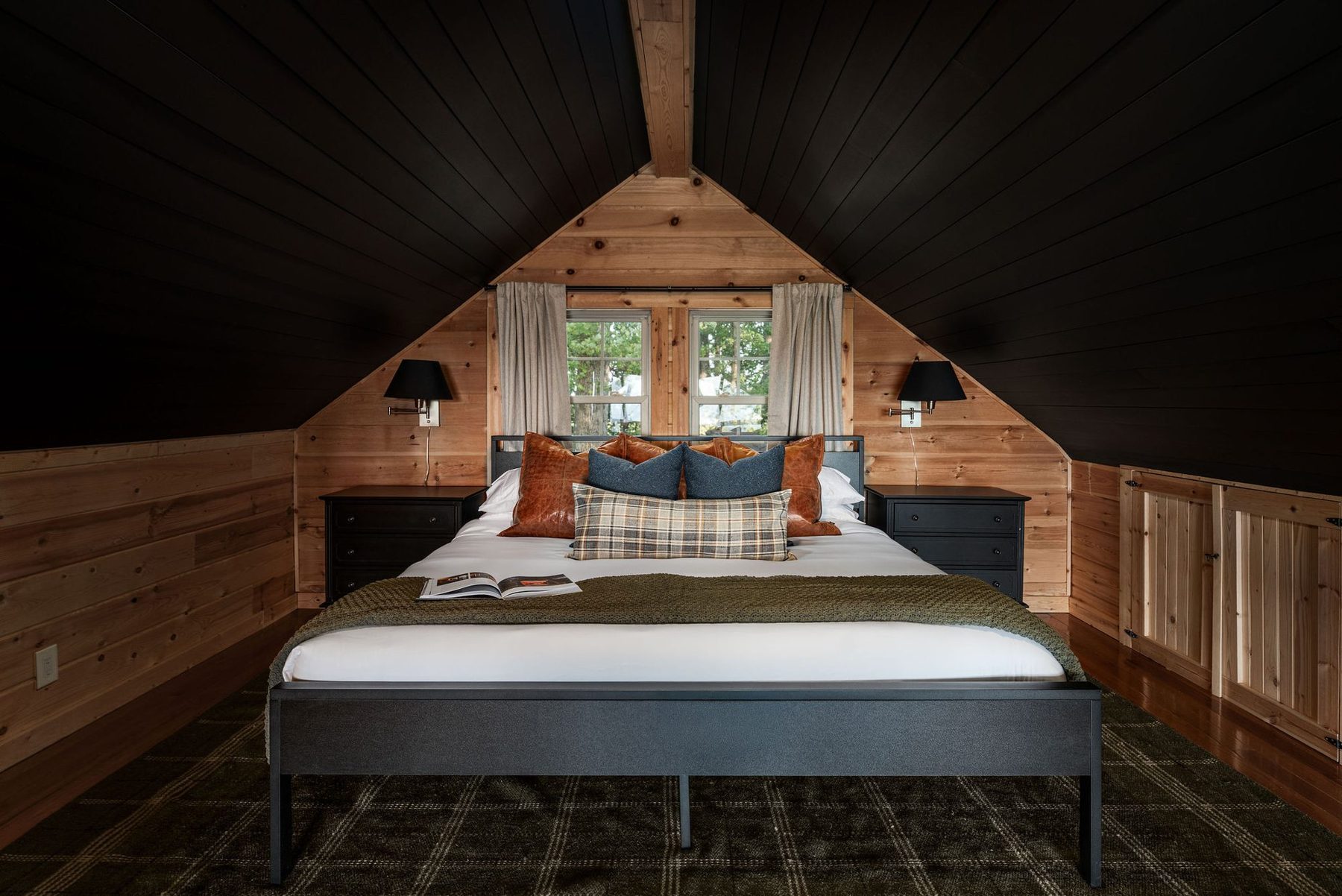 Loft bedroom tucked under the black-painted roof pitch, with rust and navy cushions