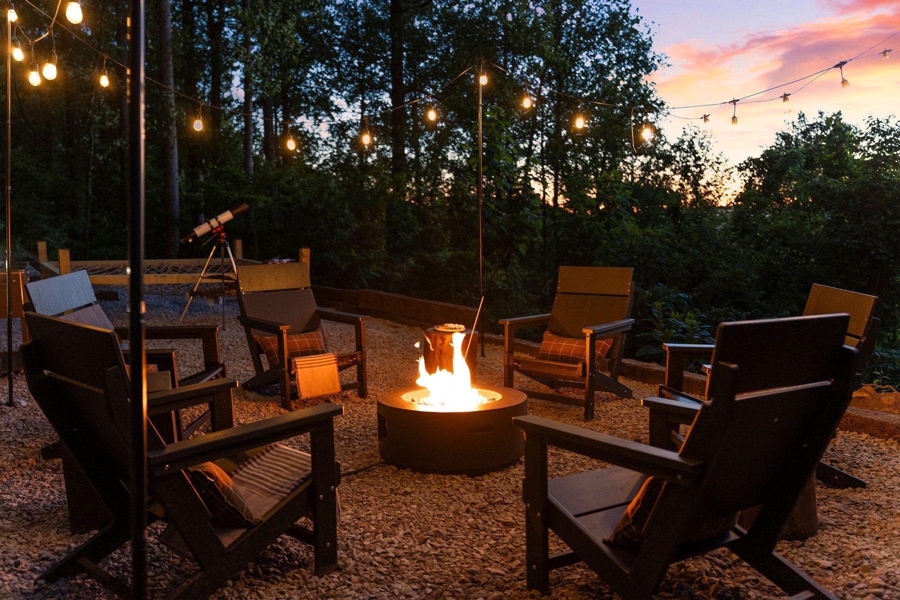 Fire pit circle with Adirondack chairs under festoon lights at dusk