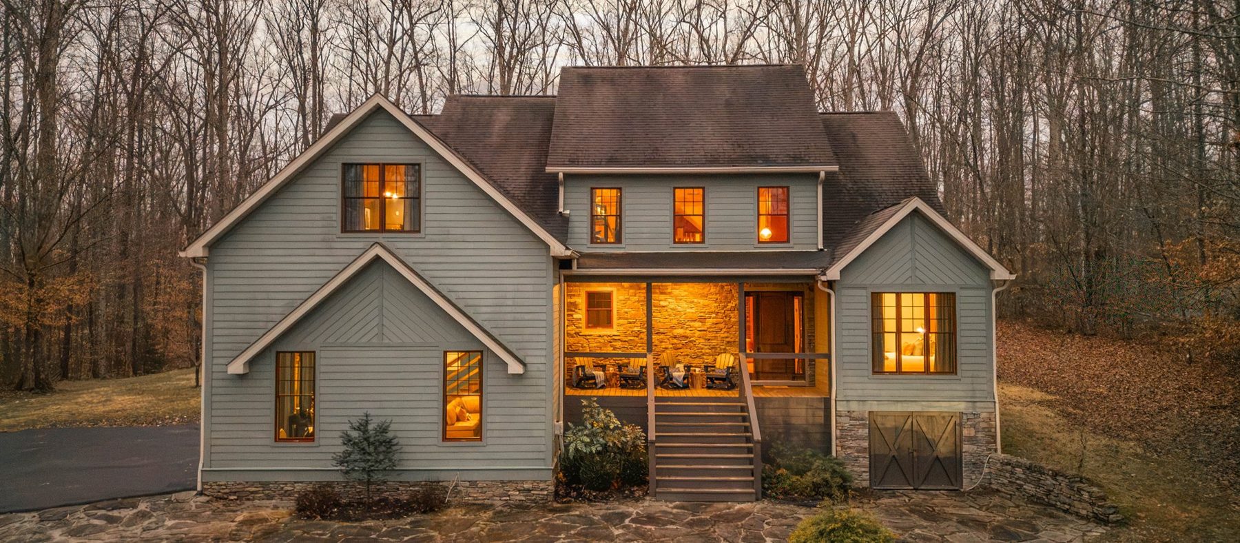 Mountain Mama Modern at twilight, a sage clapboard house with a glowing stone porch