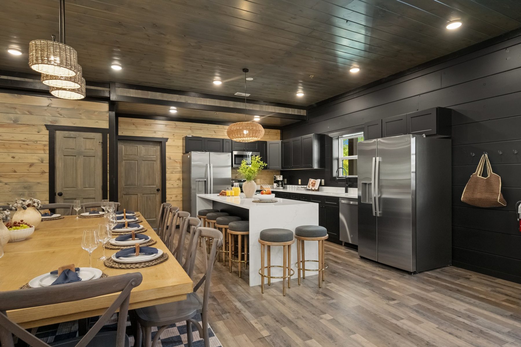 Open-plan view from the long dining table through to the kitchen island, under a dark plank ceiling