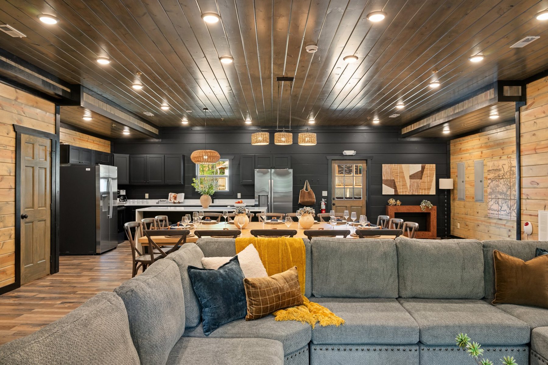 Living area with an oversized grey sectional, mustard throws and the kitchen beyond