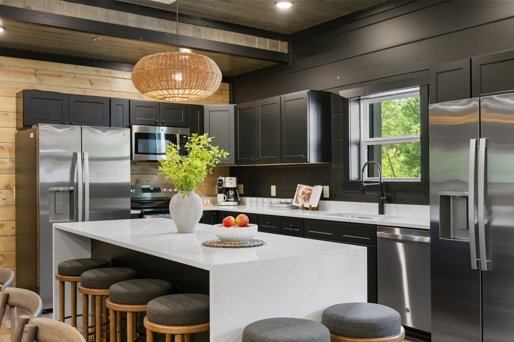 Kitchen with black shaker cabinets, a white quartz island, rattan pendant and pine accent wall