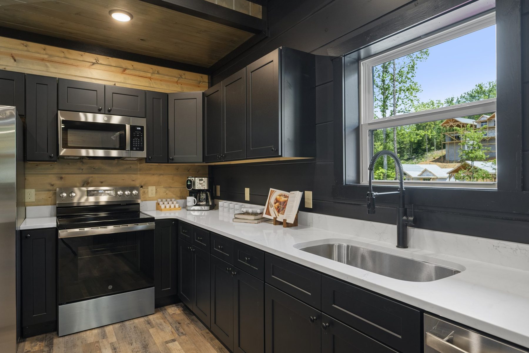 Kitchen run with stainless appliances, a window over the sink and a cookbook on the counter