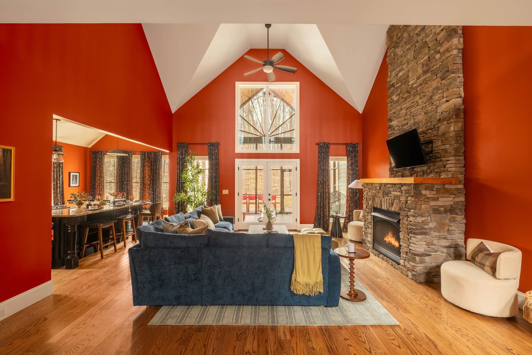 Vaulted great room in rust red with a stacked-stone fireplace and navy velvet sectional