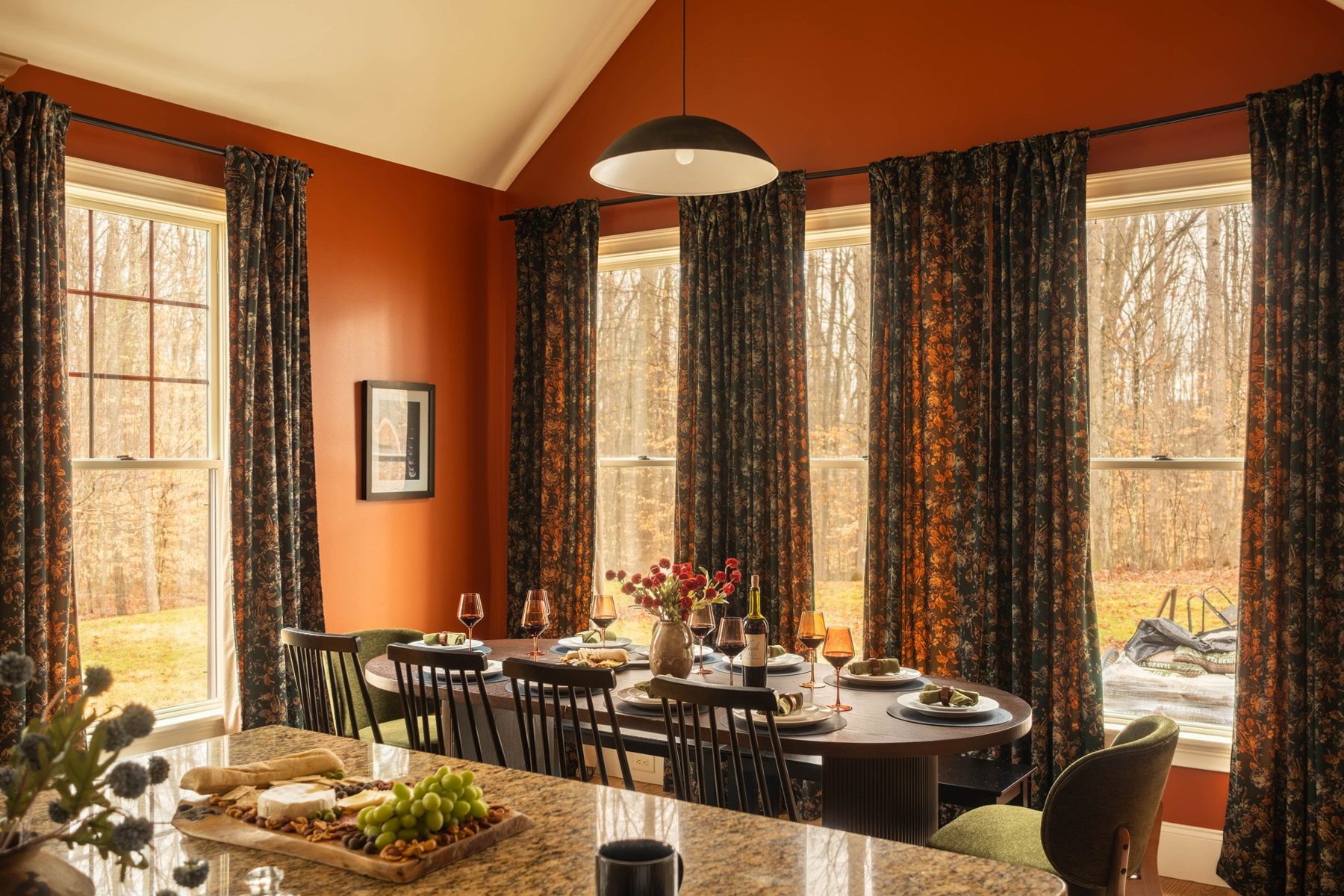 Dining room with a black pendant, patterned drapes and a long table set for guests
