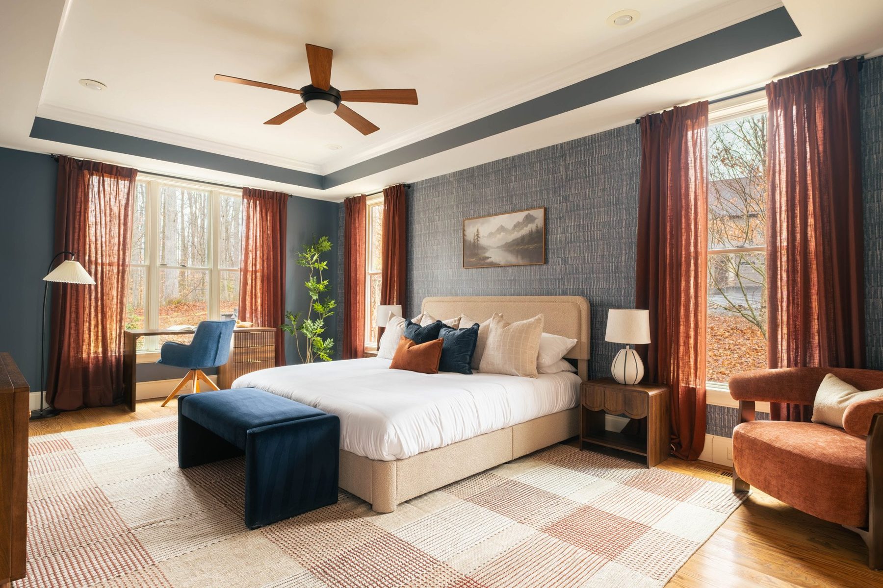 Primary bedroom with deep navy walls, rust linen curtains and a plaid rug