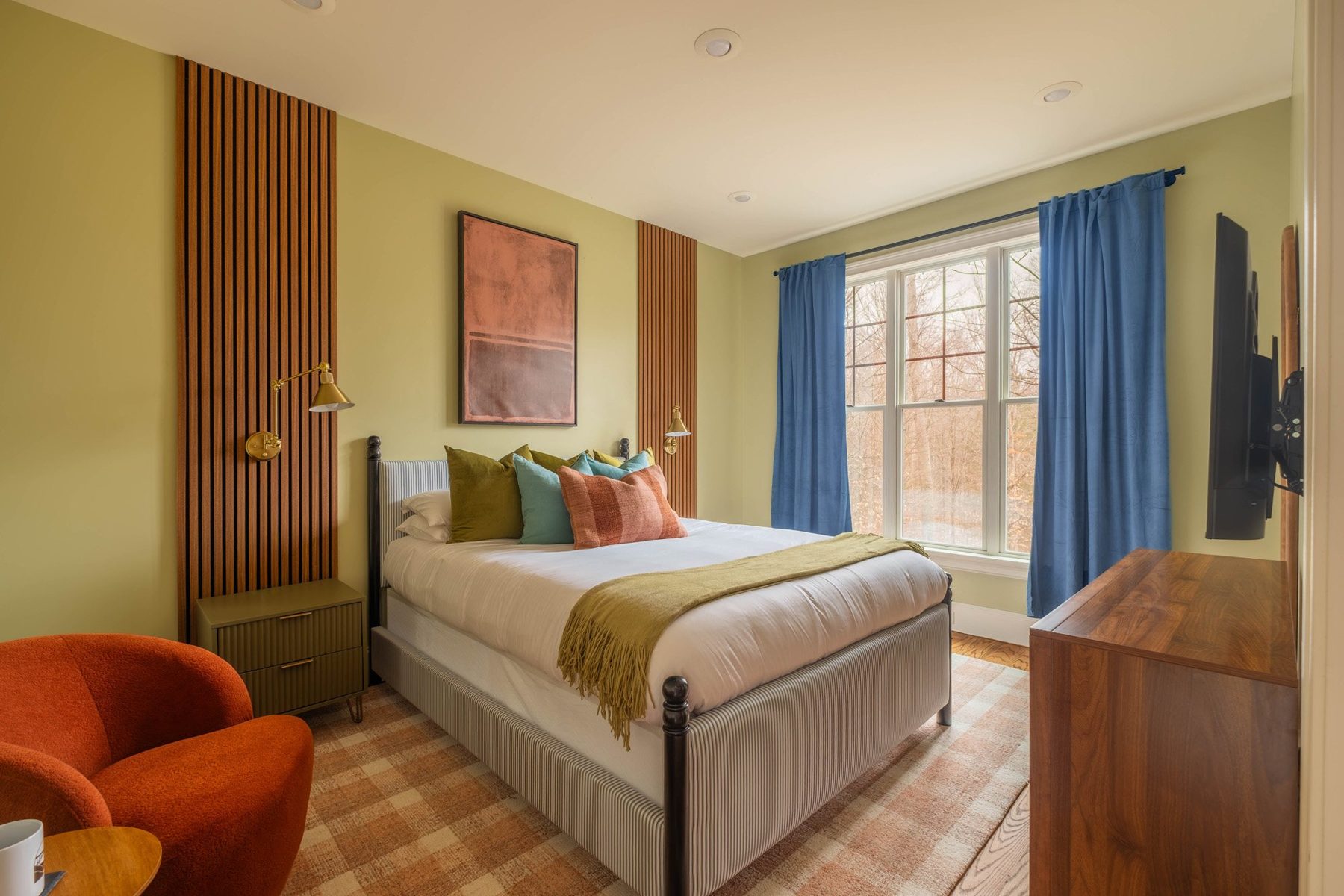 Guest bedroom with a chartreuse wall, walnut slat panels and blue curtains