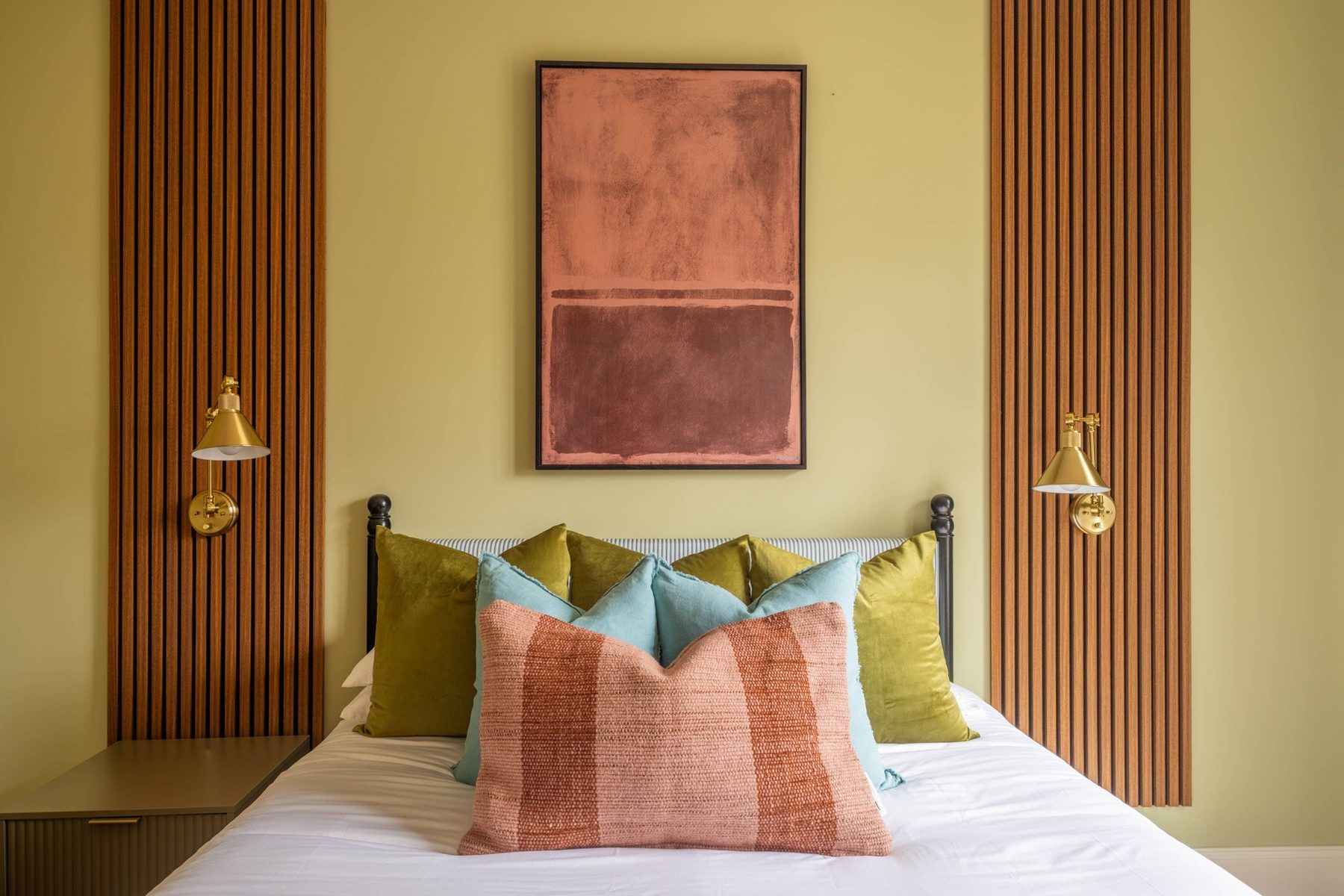 Guest bed with brass wall lights, slat panels and a rust abstract artwork