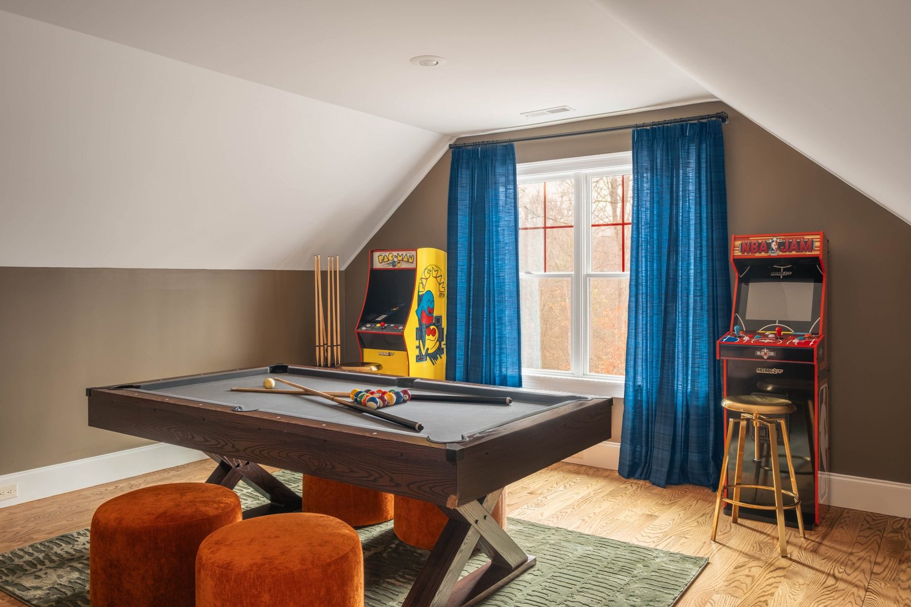 Games loft under the eaves with a pool table, arcade cabinets and blue curtains