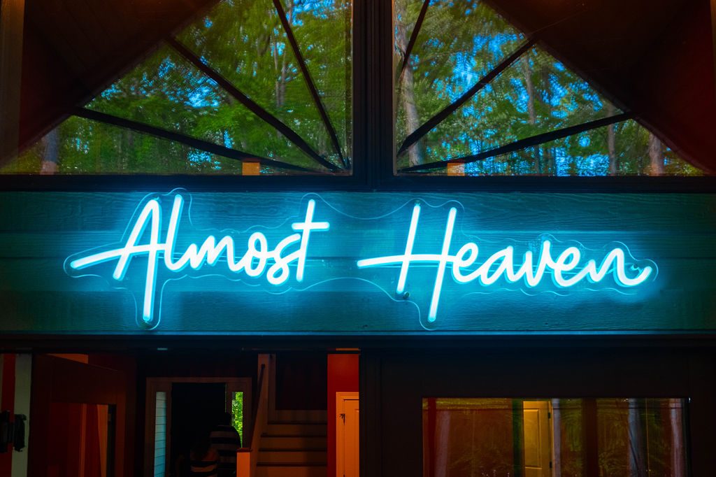Almost Heaven neon script glowing beneath the porch gable at night