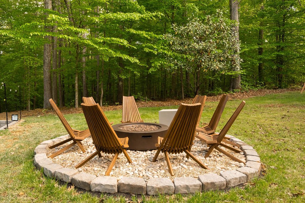 Stone fire pit circle ringed with timber lounge chairs in the woods