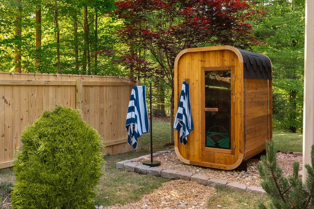 Cedar barrel sauna on a pebble pad among the trees, with navy and white striped towels