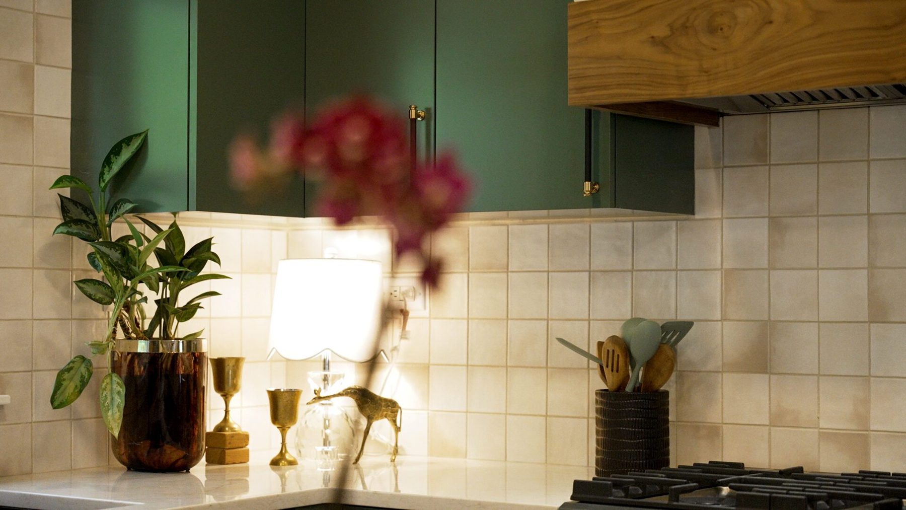 Handmade-look cream tile splashback with brass accents, plants and an orchid under the walnut-banded hood