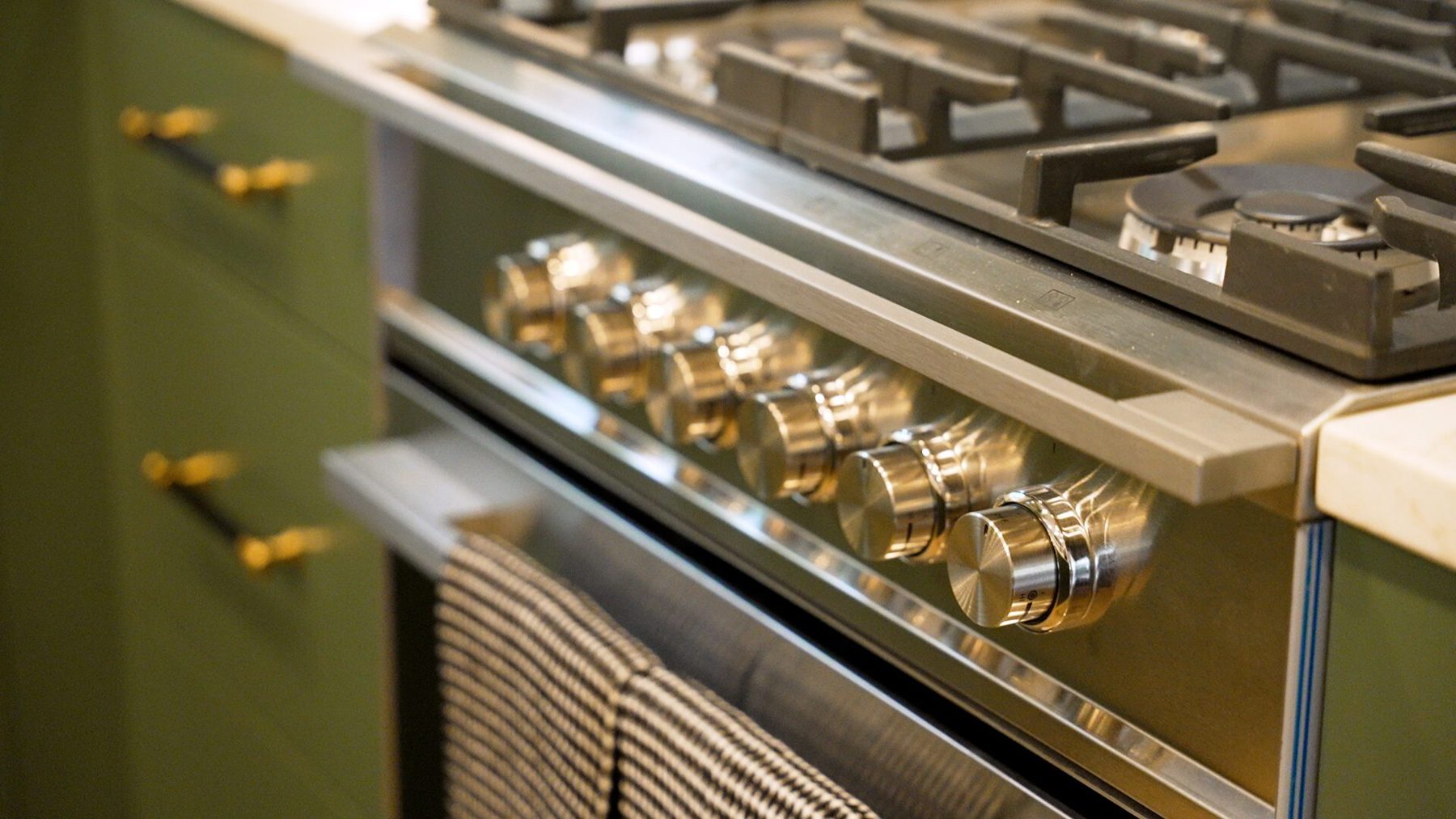 Close-up of the range knobs and brass bar pulls on sage green drawers
