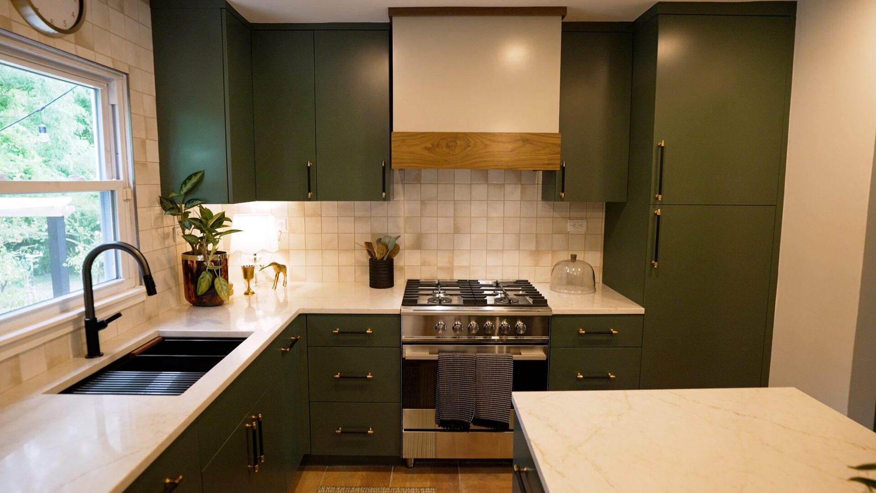 The cooking wall: range, plaster hood with walnut band and sage green cabinets